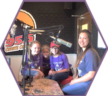 Three campers and a camp counselor participate are pictured n the recording booth of a radio station.