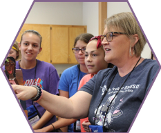 A SAGE STEAM workshop presenter assists three campers with a computer programming problem.